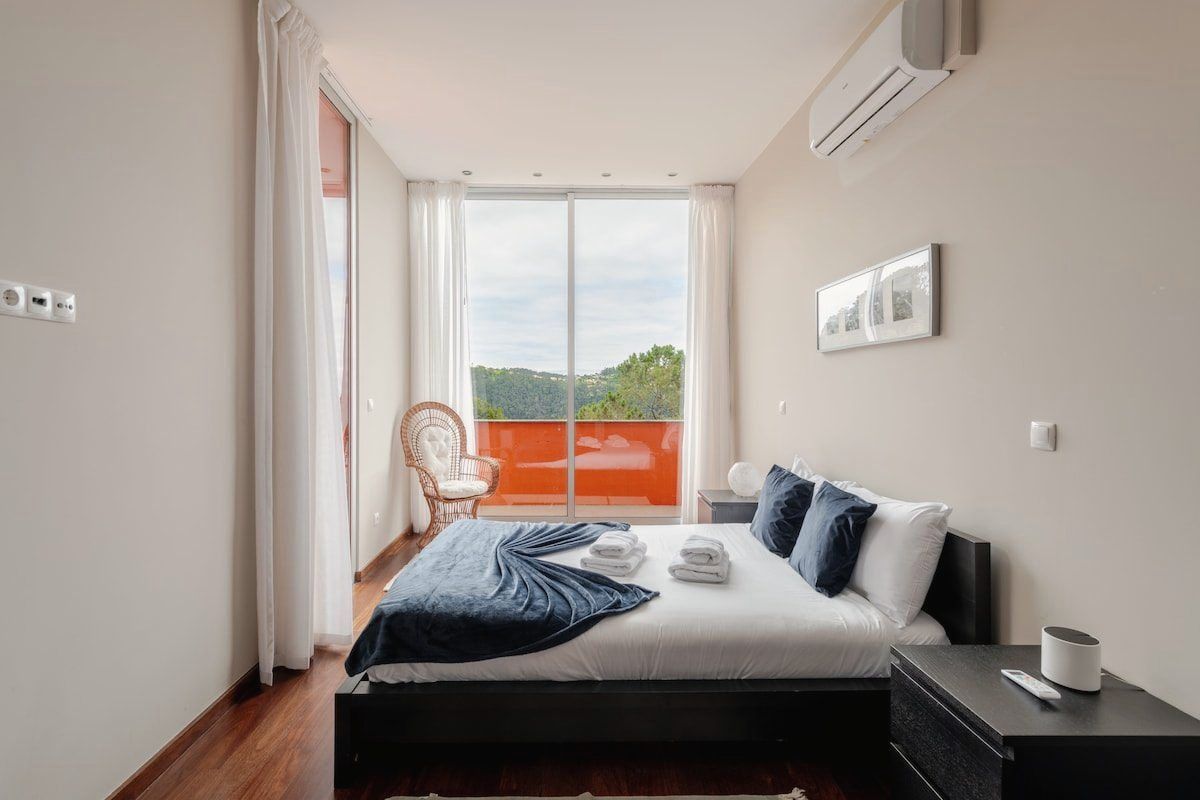 Guest bedroom with a queen bed, the orange terrace wall beyond the glass