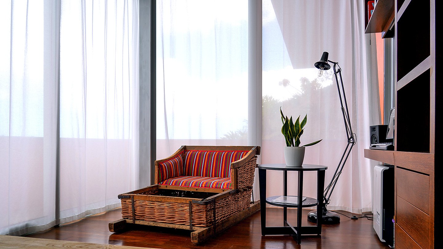 A traditional Madeiran wicker toboggan, turned into a seat with a striped cushion, by the sheer curtains