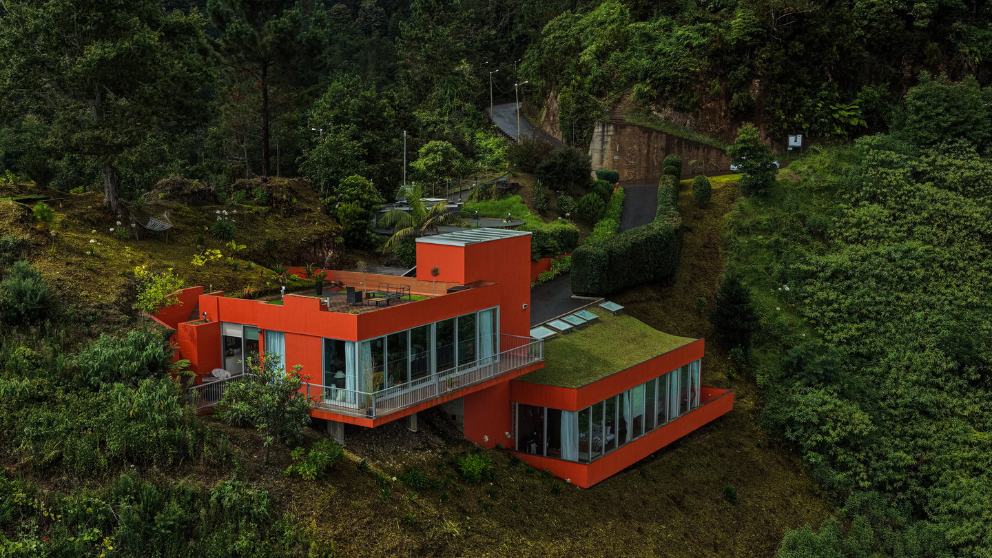 The villa from the air: orange volumes stepped into the hillside, glazed on two sides, under a planted roof